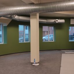 MAT-HOUSE Wykończenia Wnętrz MATEUSZ WALESIUK - Wnętrze komercyjne po świeżym pomalowaniu ścian na biało i oliwkowo-zielono, z widocznymi kanałami wentylacyjnymi pod sufitem i przygotowanym podłożem pod nową podłogę.