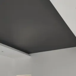 Częściowo pomalowany sufit w kolorze grafitowym z widocznymi otworami na oświetlenie punktowe i wystającymi przewodami.