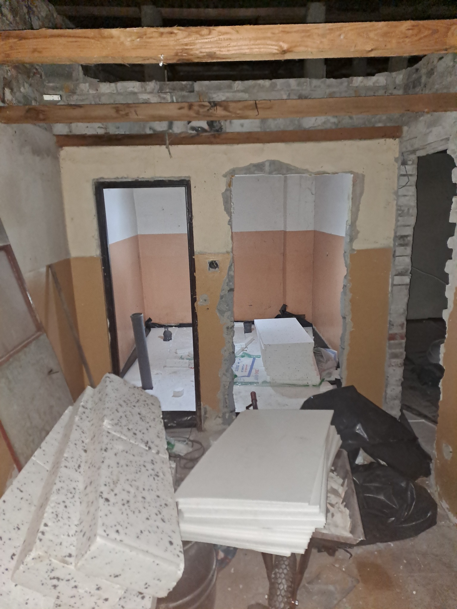 Wnętrze w trakcie remontu: widoczne niezabezpieczone belki stropowe, usunięte fragmenty ścian, przygotowane płyty styropianowe i worki na gruz.