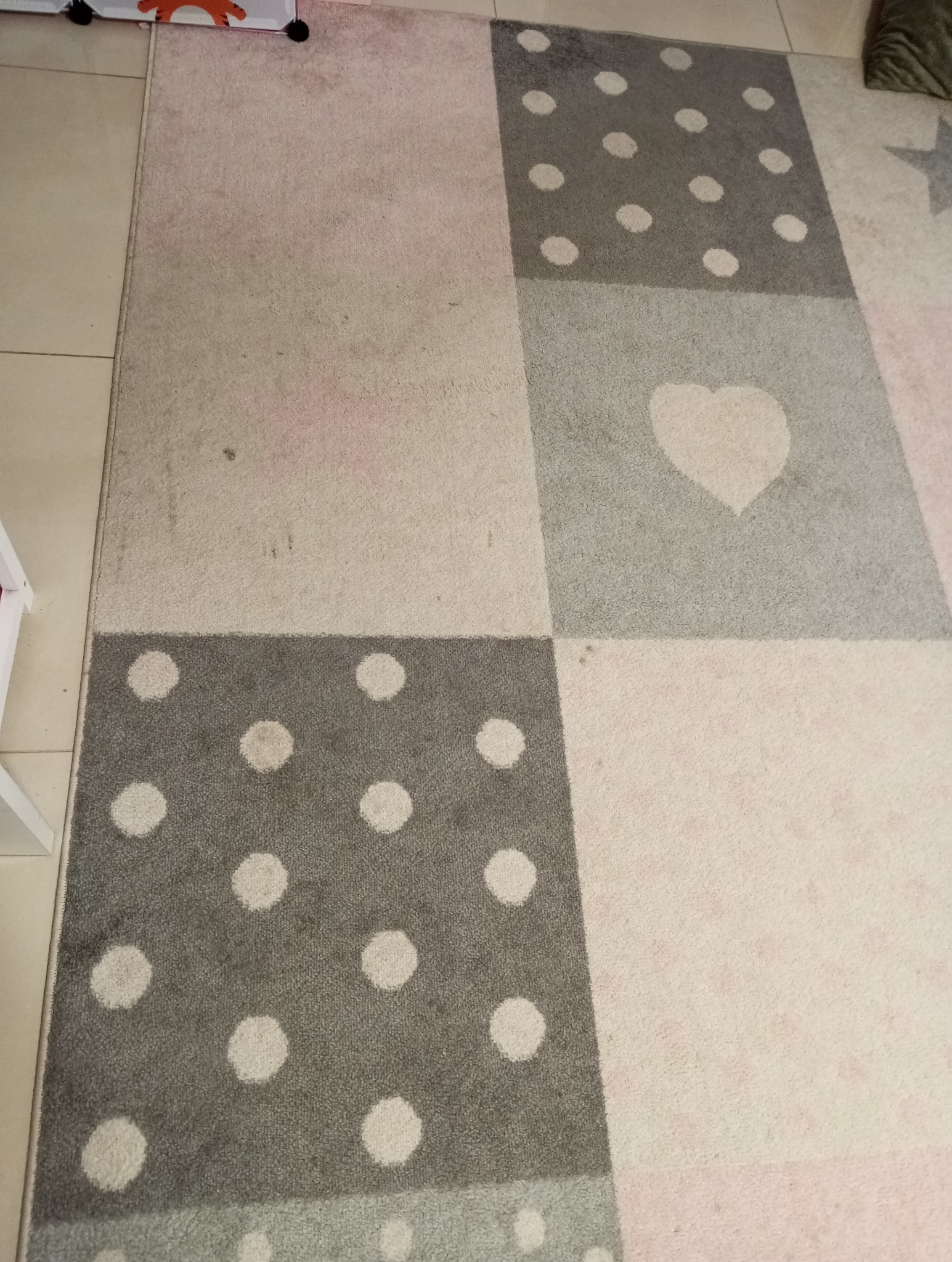 Wielokolorowy dywan dziecięcy w geometryczne wzory, widoczne plamy i zabrudzenia na jasnym tle.
