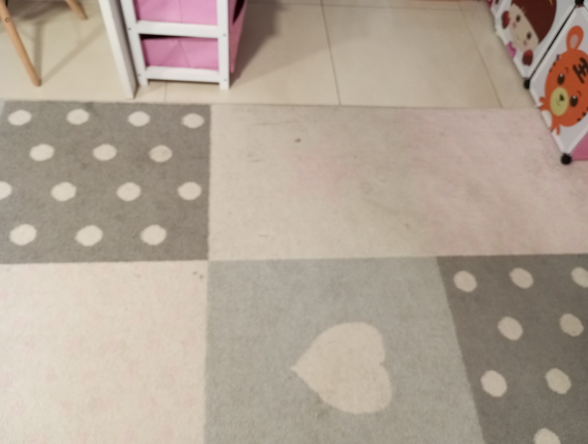 Fragment wzorzystego dywanu dziecięcego w pokoju, widoczne szare kwadraty z białymi kropkami i białym sercem, obok meble dziecięce.