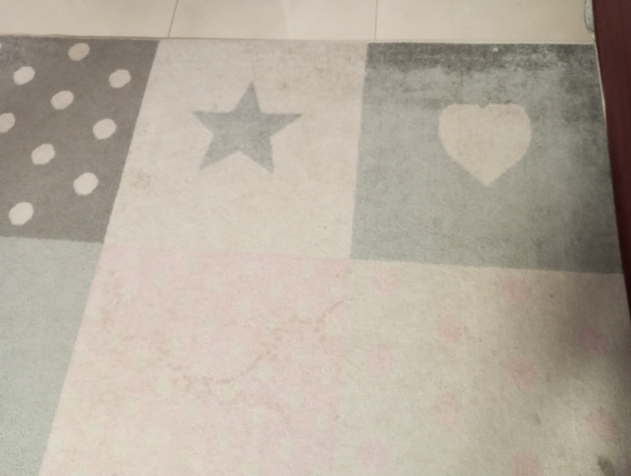 Wzór dywanu z szarymi figurami: gwiazda, serce i kropki, widoczne ślady użytkowania.