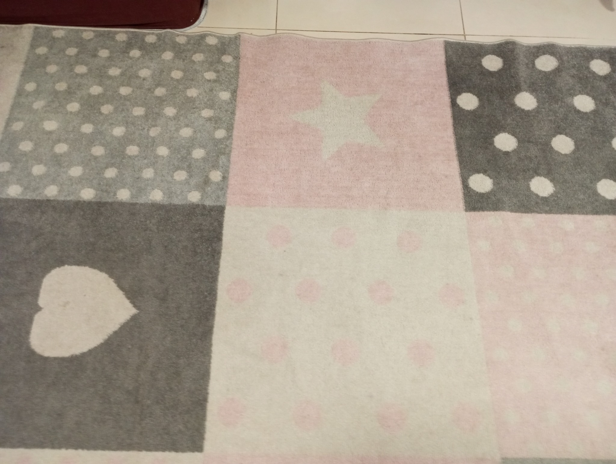 Wielobarwny dywan dziecięcy z motywem serca, gwiazdy i kropek na jasnych płytkach podłogowych.