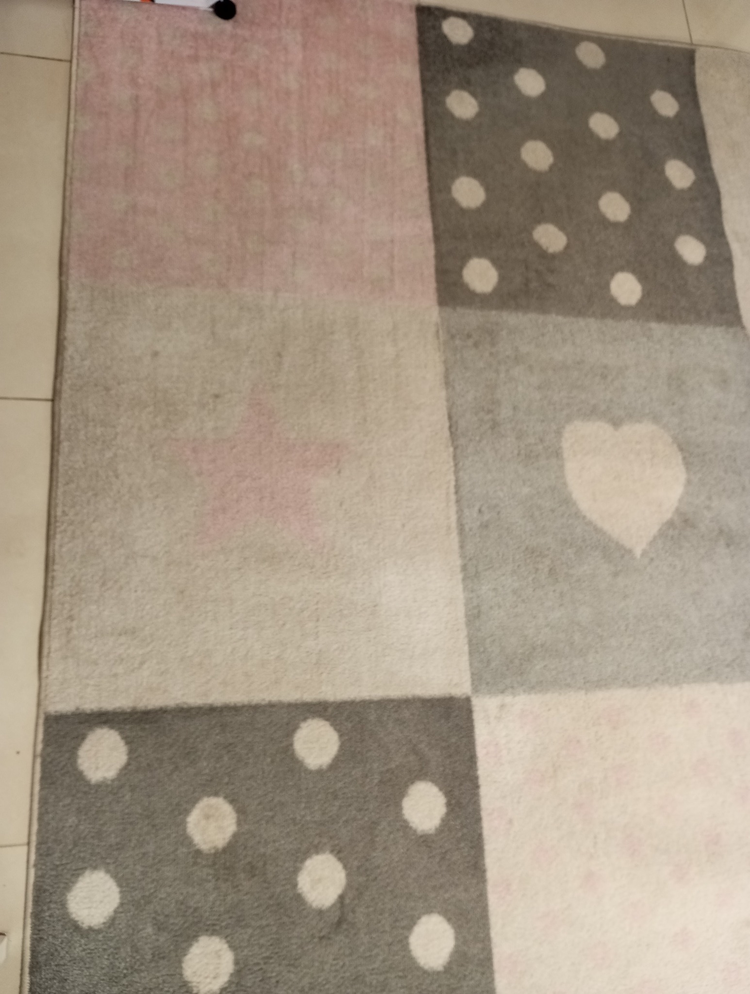 Wielobarwny dywan dziecięcy w kwadraty z wzorami: różowe i szare kwadraty, kropki i serce.