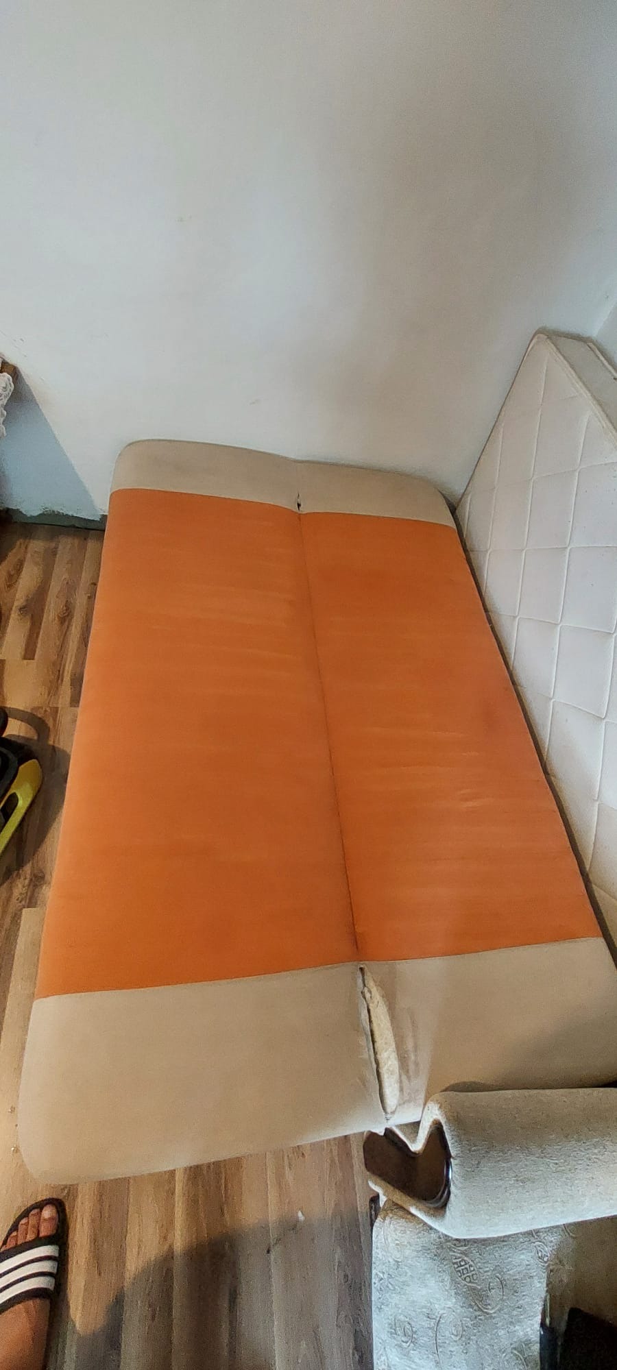 Pomarańczowa kanapa dwuosobowa z beżowymi bokami, widoczne ślady użytkowania i niewielkie uszkodzenia tapicerki przy łączeniu siedzisk.