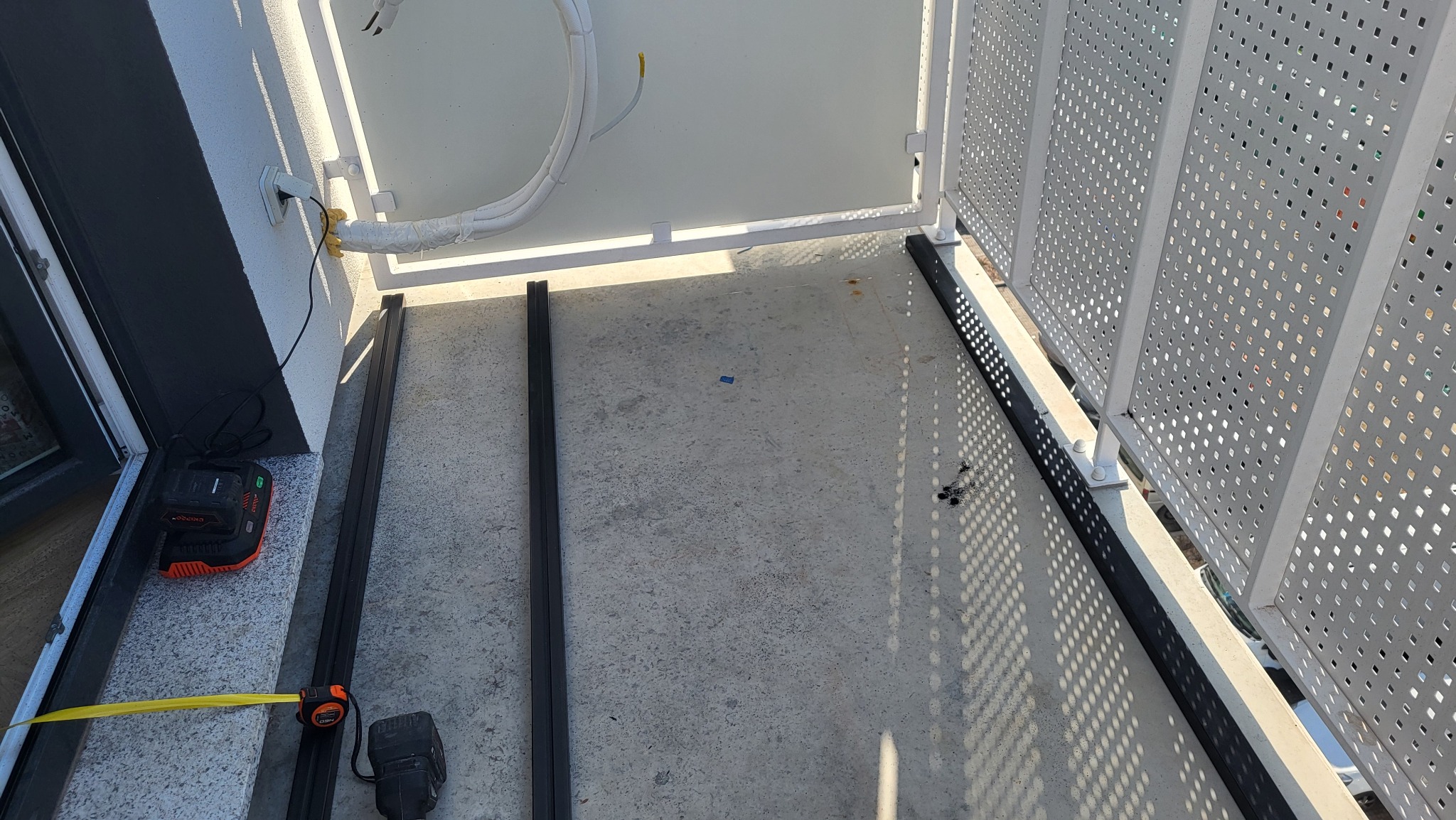 Montaż metalowej konstrukcji na balkonie z perforowaną balustradą. Widoczne narzędzia i elementy konstrukcyjne, przygotowane do dalszych prac wykończeniowych.