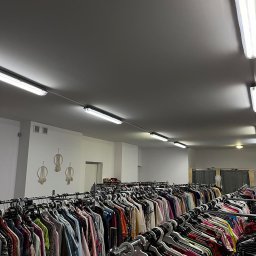 LARGO - Wnętrze sklepu z odzieżą używaną, rzędy ubrań na wieszakach, widoczne dekoracje makramowe na ścianie i oświetlenie sufitowe.