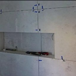 Prace Remontowo - Budowlane - Marcin Wójcik - Ściana z szarych płytek ceramicznych w trakcie montażu, z widocznymi niebieskimi klipsami poziomującymi i wnęką z narzędziami.