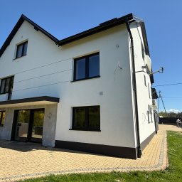 VADYM HAL DOBRO W DZIAŁANIU - Dwukondygnacyjny dom z białą elewacją i czarnymi ramami okiennymi, widziany z perspektywy ogrodu z kostką brukową. Świeżo pomalowana fasada w słoneczny dzień.