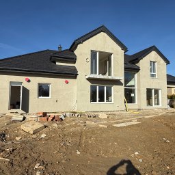 VADYM HAL DOBRO W DZIAŁANIU - Surowy stan elewacji domu jednorodzinnego w Krakowie, z widocznymi cegłami i gruzem na posesji. Dom z ciemnym dachem i jasną elewacją w trakcie prac wykończeniowych.