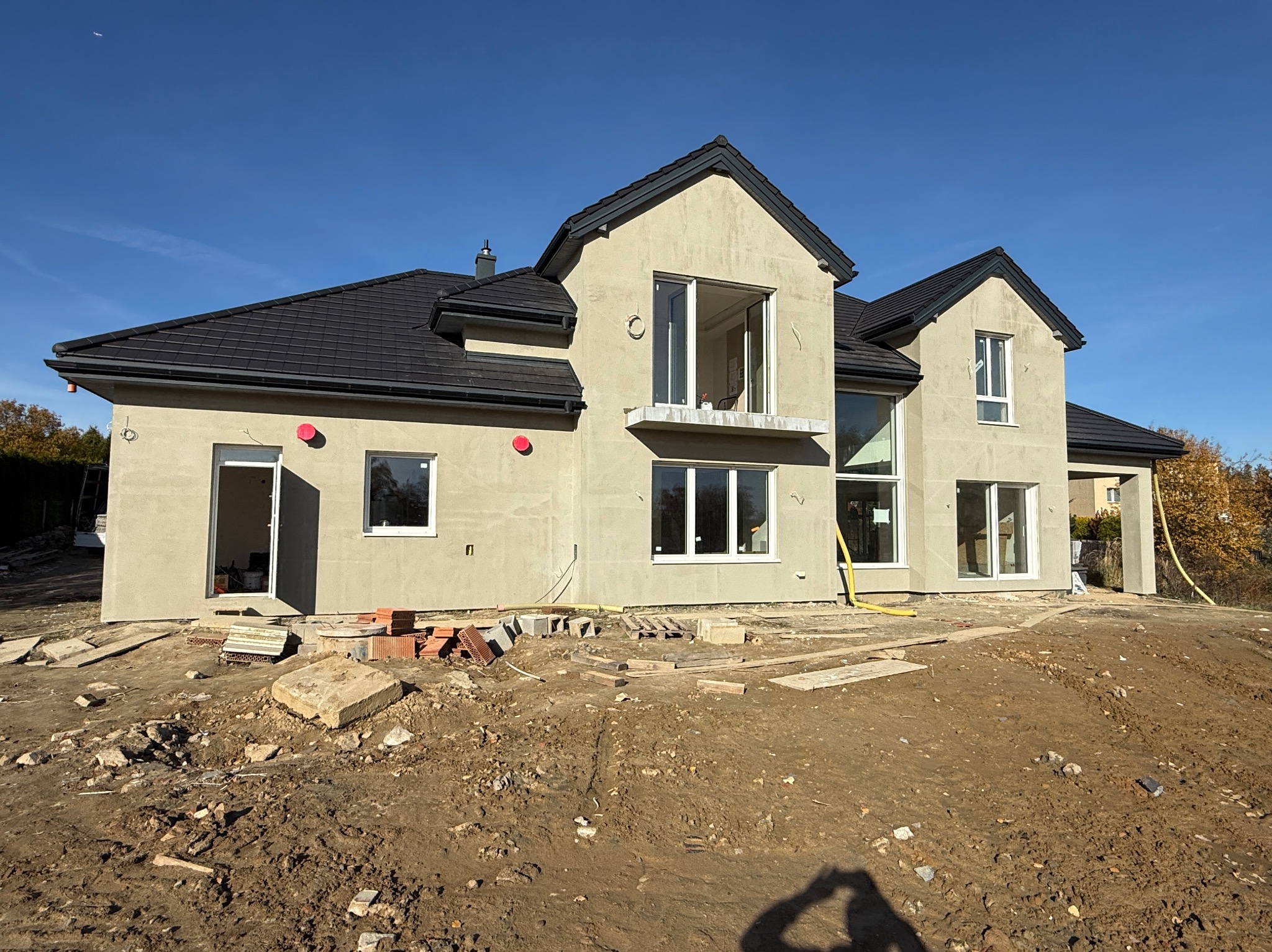 Surowy stan elewacji domu jednorodzinnego w Krakowie, z widocznymi cegłami i gruzem na posesji. Dom z ciemnym dachem i jasną elewacją w trakcie prac wykończeniowych.