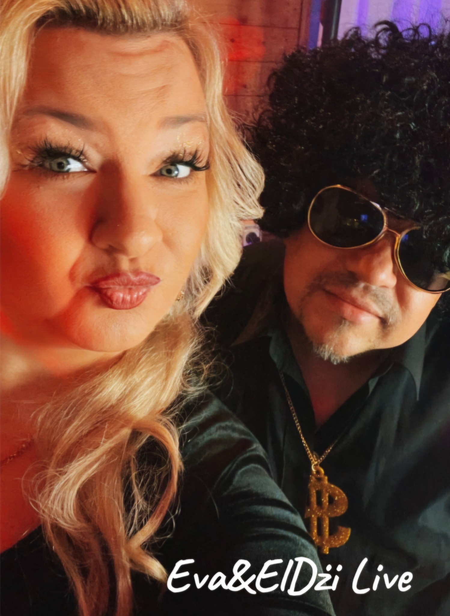 Portret duetu muzycznego Eva&ElDżi Live, z wokalistką o blond włosach i muzykiem w afro peruce i okularach, na tle drewnianej ściany.