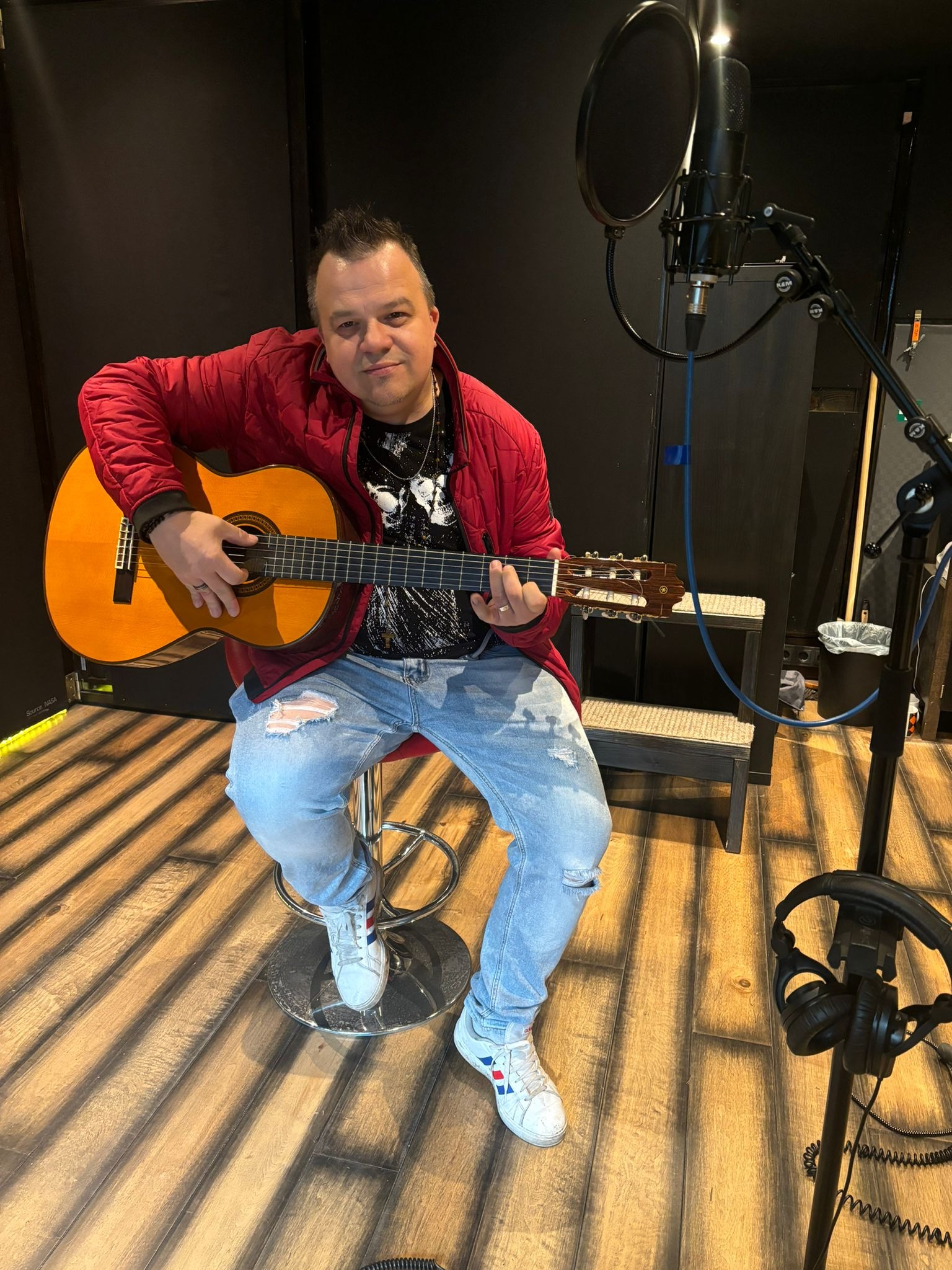 Muzyk z Geesthacht w czerwonej kurtce gra na gitarze klasycznej w studiu nagraniowym z mikrofonem i słuchawkami.