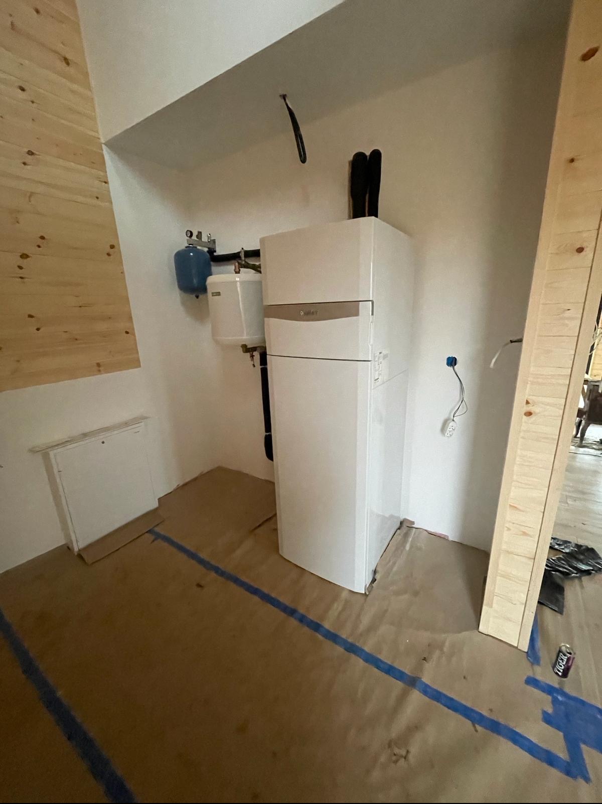 Biały, kondensacyjny piec gazowy Vaillant z zasobnikiem ciepłej wody, zamontowany w pomieszczeniu z drewnianą boazerią i zabezpieczoną podłogą.