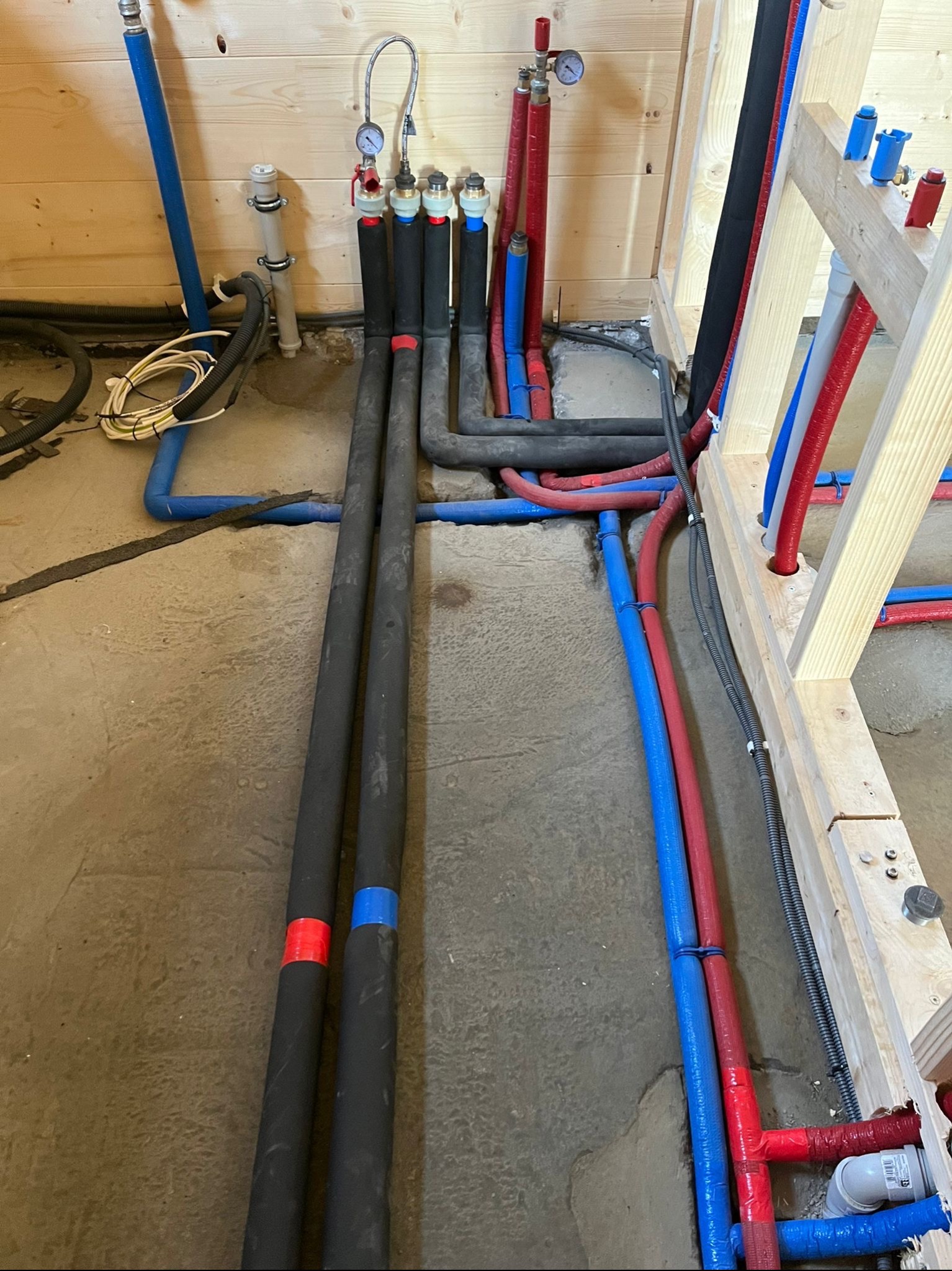 Nowa instalacja wodna i grzewcza w Sierakowicach: rury PEX w izolacji, manometry i drewniana konstrukcja szkieletowa w surowym stanie.