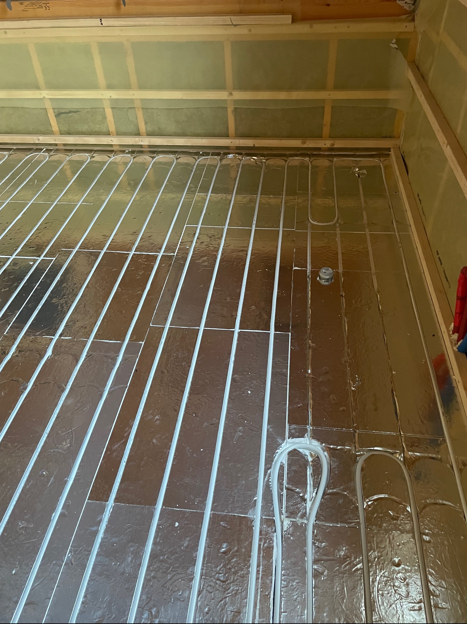 Montaż rur ogrzewania podłogowego na folii izolacyjnej, widoczne pętle rur i elementy mocujące, surowy stan wykończenia wnętrza.