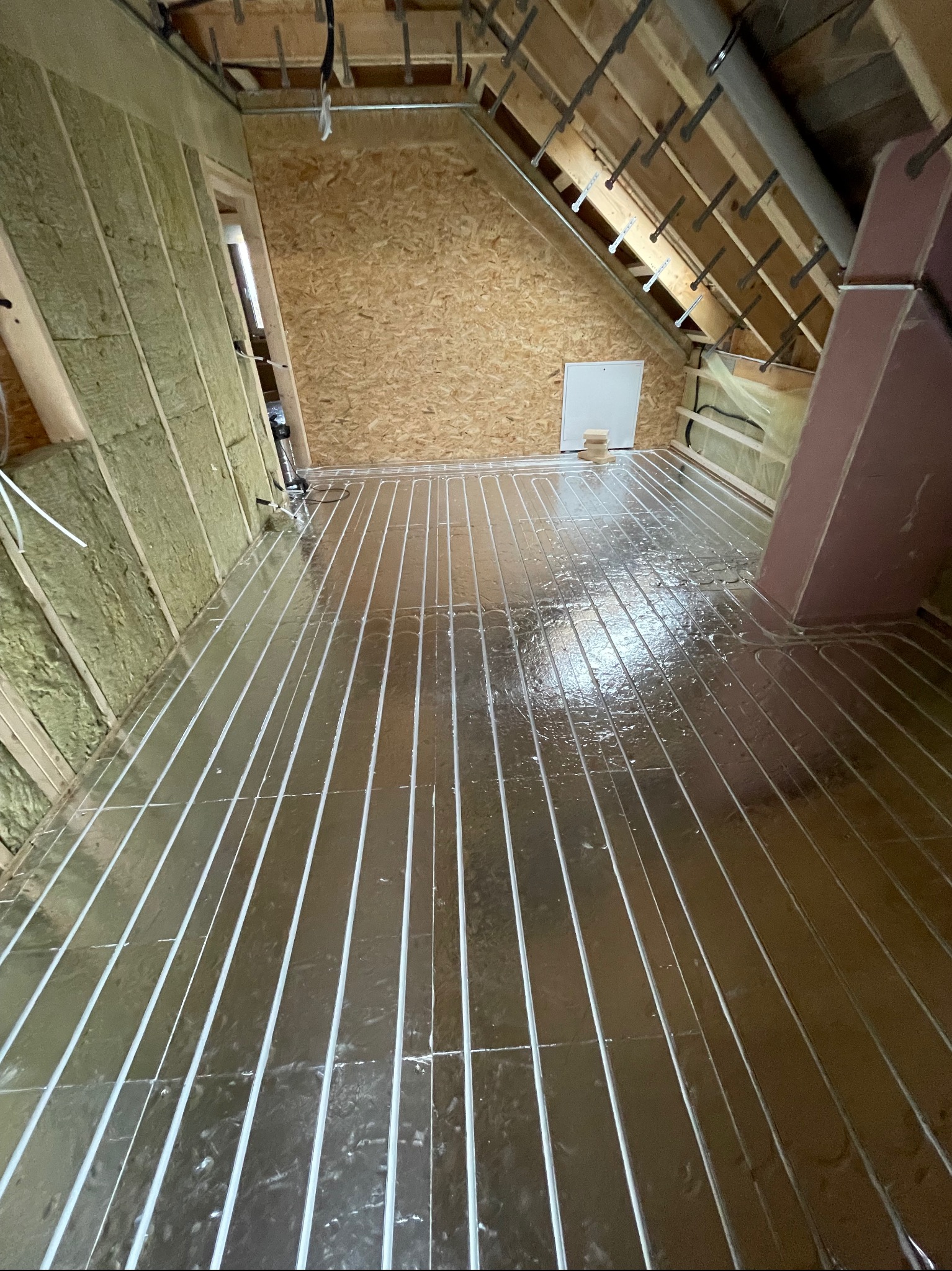 Montaż ogrzewania podłogowego w nowym domu: widok na błyszczące rury grzewcze ułożone na izolacji, ściany wyłożone wełną mineralną, surowy strop z widocznymi elementami konstrukcyjnymi.