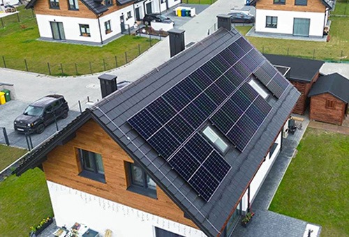 Dom jednorodzinny z panelami słonecznymi na dachu, widok z góry, czarny samochód na podjeździe, dach pokryty grafitową dachówką.