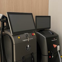 KOSMETOLOGIA ESTETYCZNA PIED-DE-POULE - Dwa urządzenia do zabiegów laserowych, model Soprano Titanium i Harmony XL PRO, ustawione obok siebie w gabinecie, z widocznymi panelami dotykowymi i głowicą lasera.