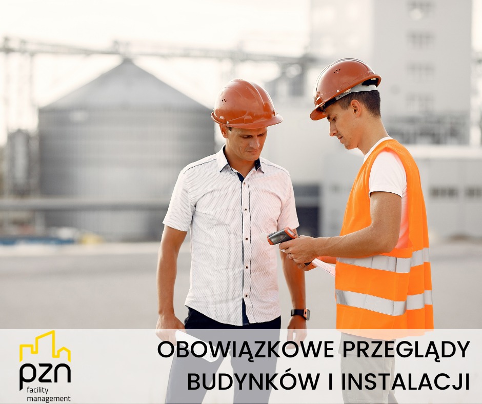 Dwóch inżynierów w kaskach kontroluje instalacje przy pomocy miernika na tle przemysłowego budynku. Obowiązkowe przeglądy budynków i instalacji.