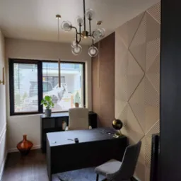 Nowoczesne biuro domowe z dekoracyjną ścianą 3D w geometryczne wzory, czarnym biurkiem, szarą podłogą i designerską lampą sufitową z przezroczystymi kulami.