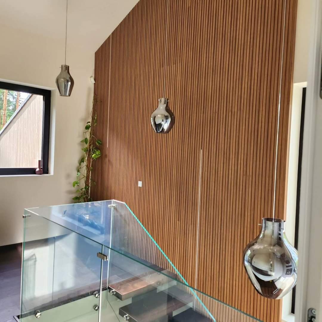 Nowoczesne wnętrze z drewnianą ścianą z lameli, szklaną balustradą schodów i wiszącymi chromowanymi lampami o kształcie wazonu, widok z góry schodów.