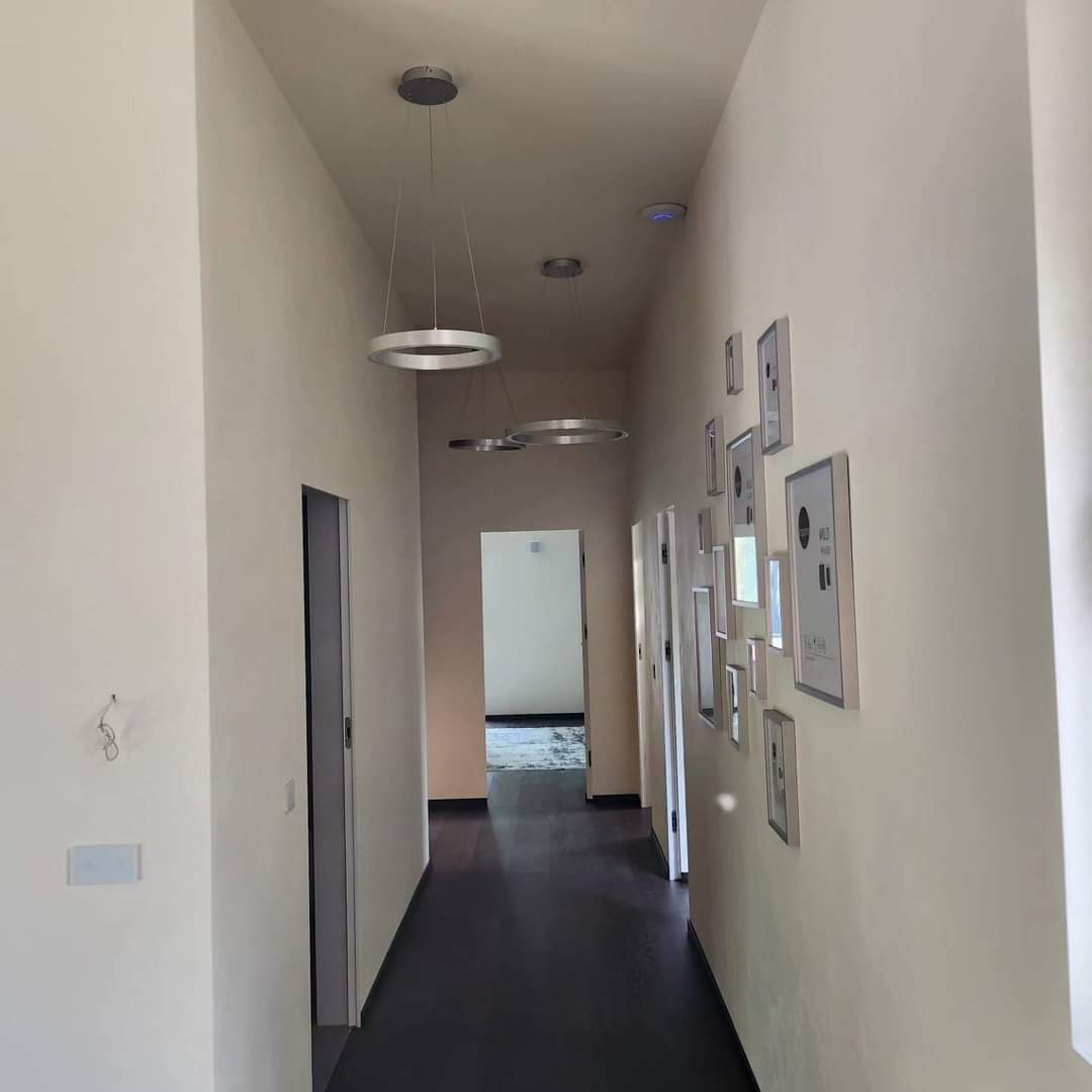 Nowoczesny korytarz z ciemną podłogą, kremowymi ścianami, okrągłymi lampami wiszącymi i galerią ramek na ścianie.