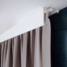 Fabryka Designu - sztukateria, szyny karniszowe, maskownice, firany, zasłony - Nowoczesny karnisz sufitowy z oświetleniem LED i zasłonami w odcieniach szarości na tle ciemnej ściany.