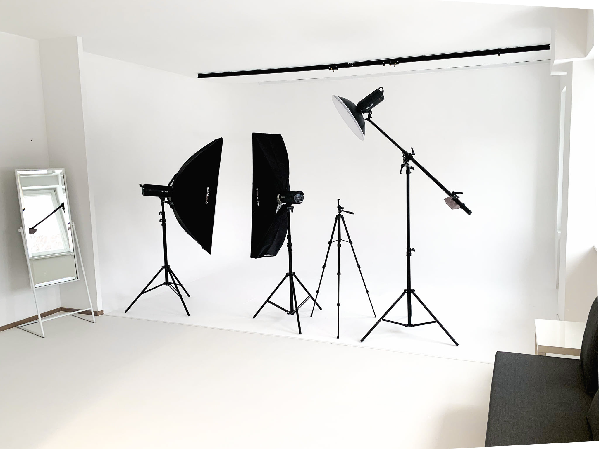 Puste studio fotograficzne z białym tłem, trzema lampami studyjnymi z softboxami i parasolką, lustrem i sofą.