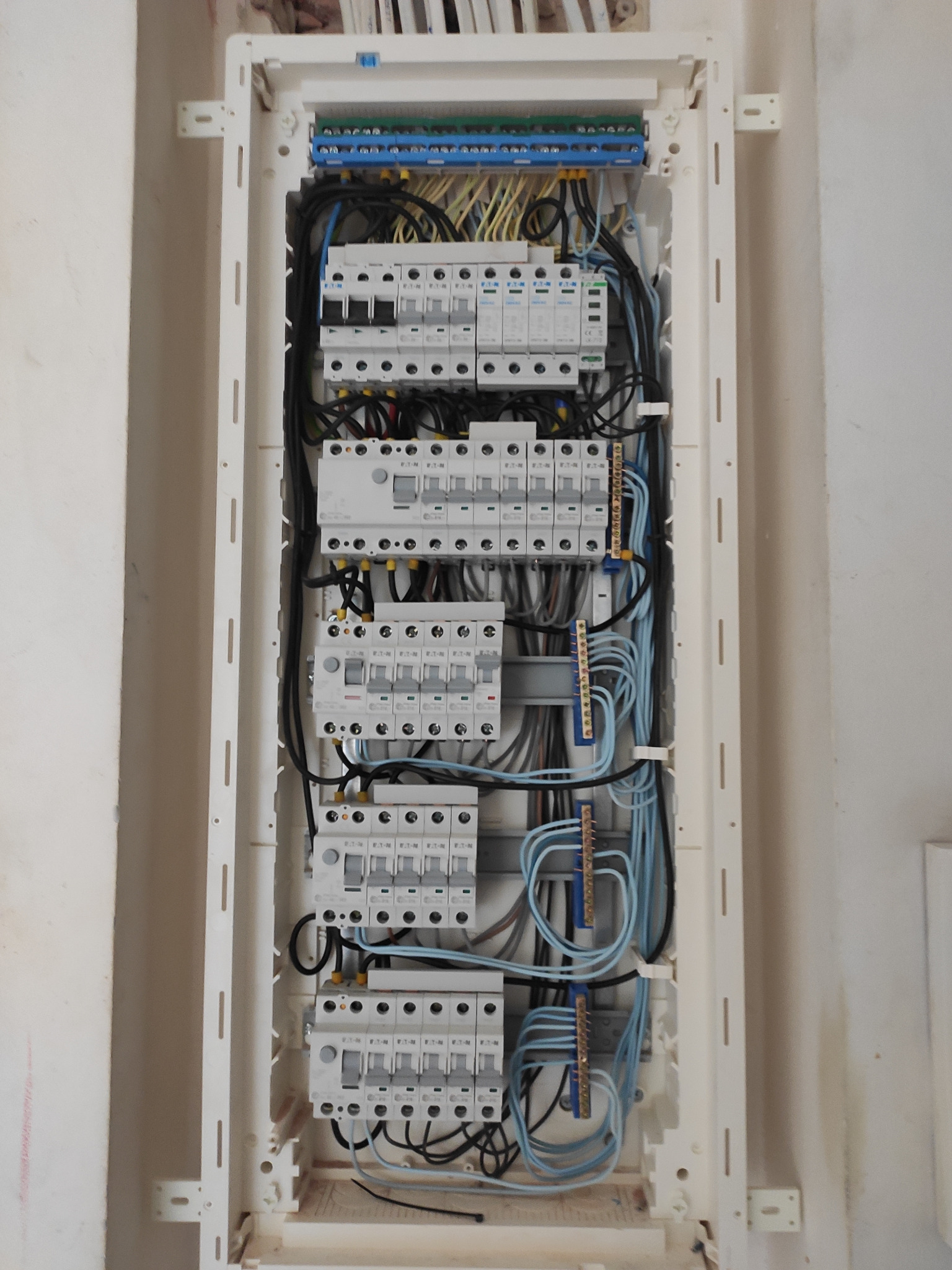 Rozdzielnica elektryczna z zamontowanymi bezpiecznikami, przewodami i listwami zaciskowymi w białej obudowie, widok z bliska na ścianie w trakcie montażu.