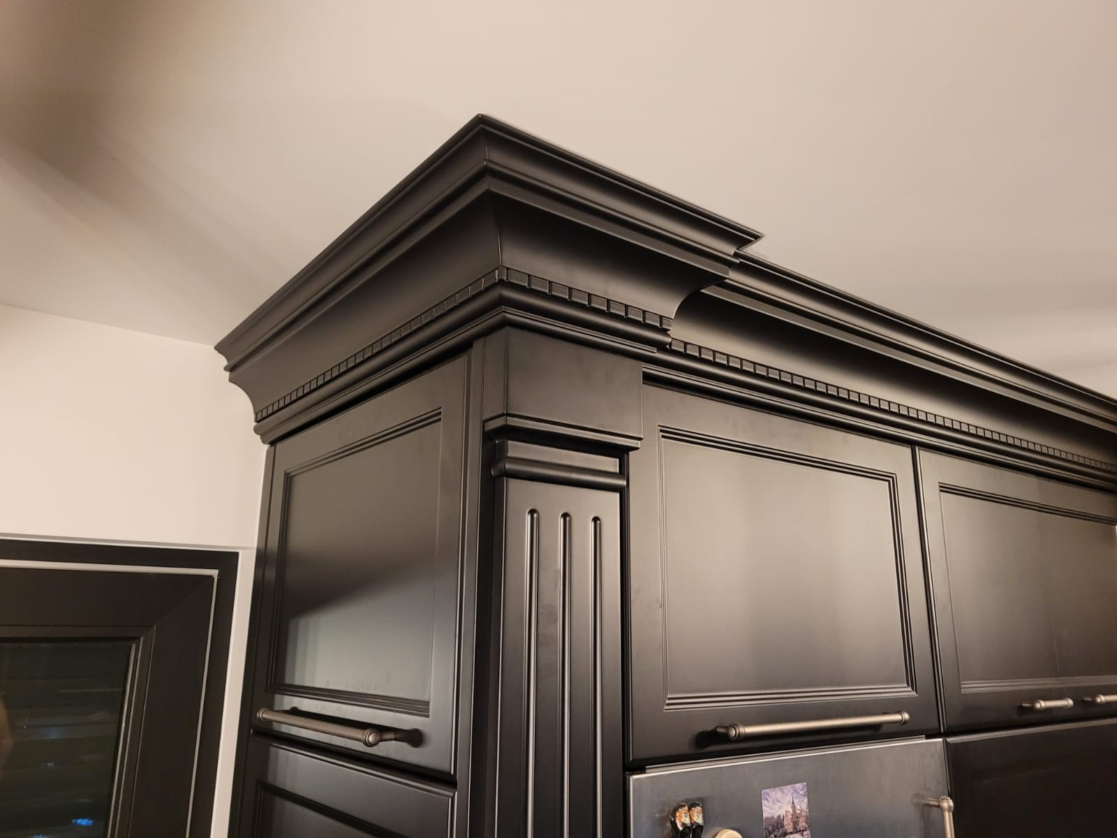 Szczegółowe ujęcie górnej części czarnych, fornirowanych szafek kuchennych z dekoracyjnymi listwami i uchwytami, widoczne z dołu pod kątem.