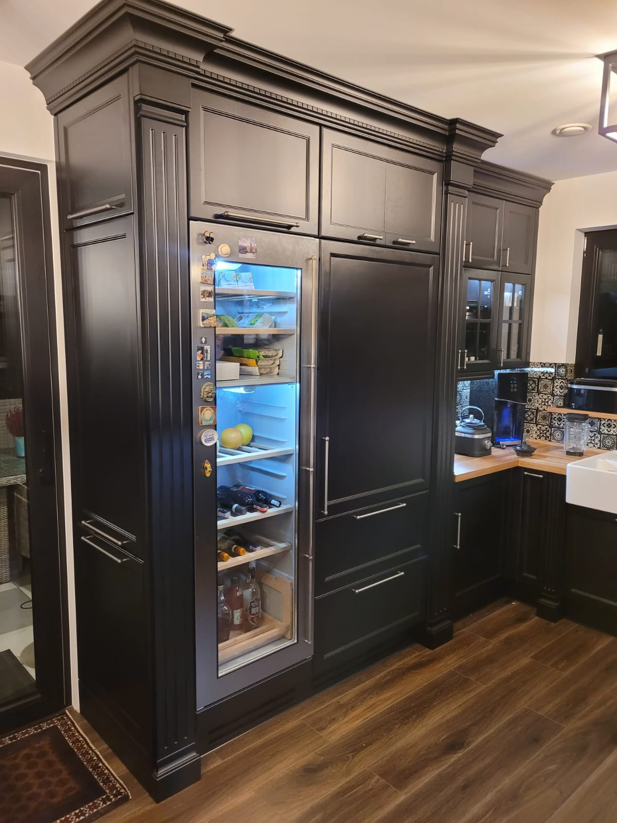 Czarna zabudowa kuchenna z lodówką na wino, widoczne detale frezowania frontów i dekoracyjne listwy wieńczące.