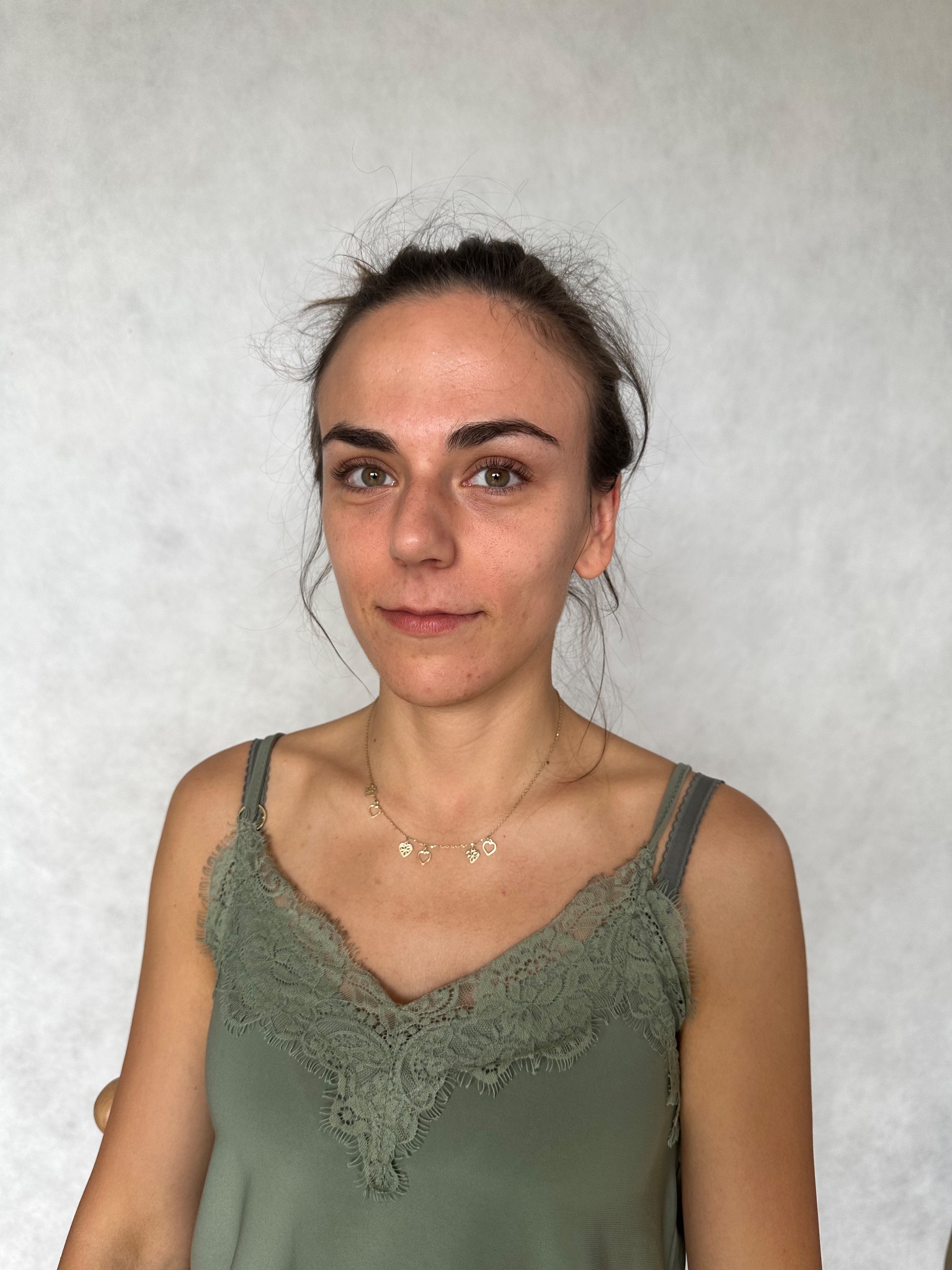 Portret kobiety z delikatnym, naturalnym wyglądem, przed zabiegiem upiększającym, z widoczną złotą biżuterią na szyi.