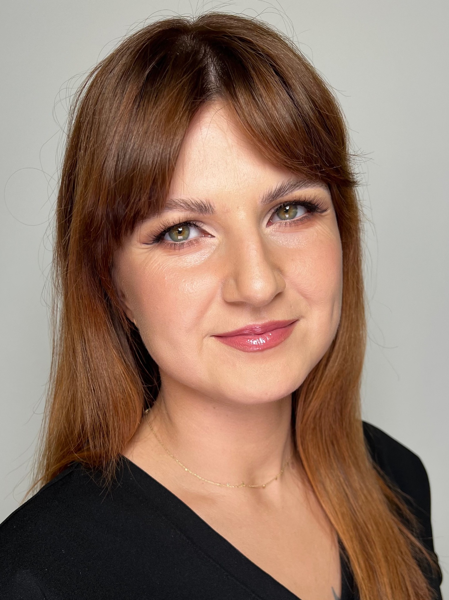 Portret kobiety z delikatnym, rozświetlonym wykończeniem, uwydatniającym zielone oczy i błyszczące usta, na jasnym tle.