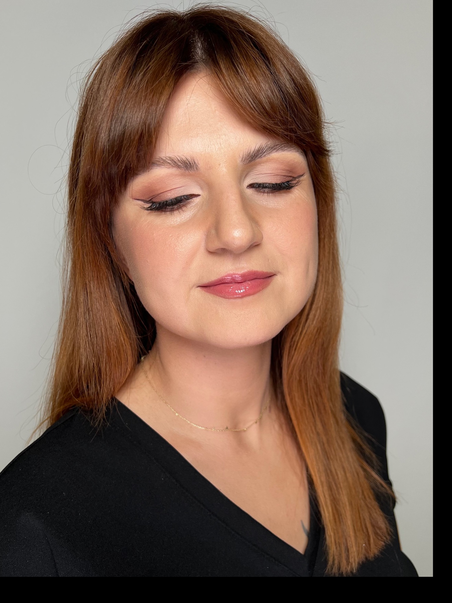 Portret kobiety z zamkniętymi oczami, prezentujący subtelny, dzienny wygląd z delikatnym cieniem na powiekach i precyzyjną kreską eyelinerem, uzupełniony błyszczącymi ustami i złotym naszyjnikiem.