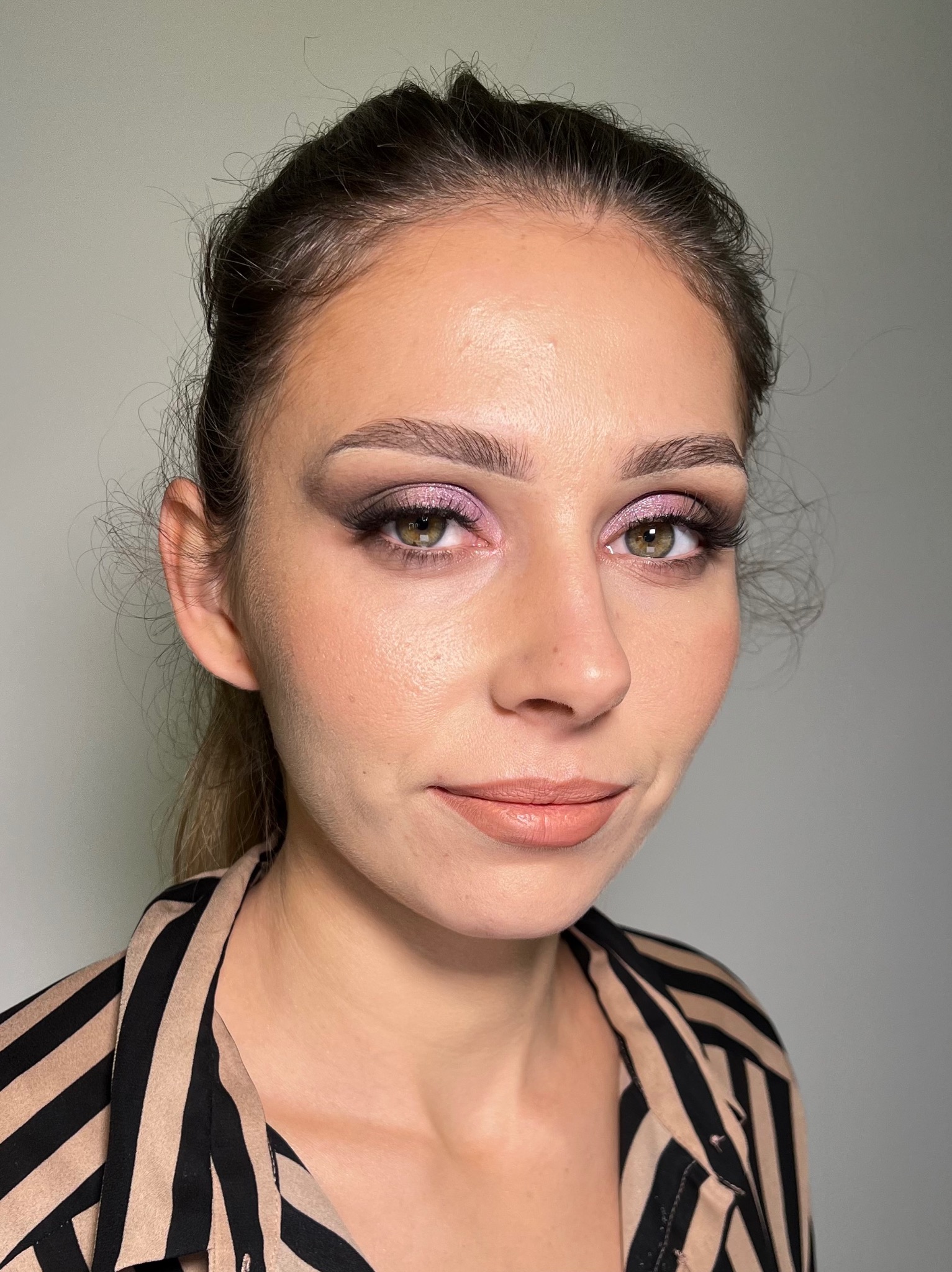 Portret kobiety z delikatnym, różowym cieniem do powiek i wydłużonymi rzęsami, w bluzce w czarno-beżowe paski, z włosami upiętymi w luźny kok.