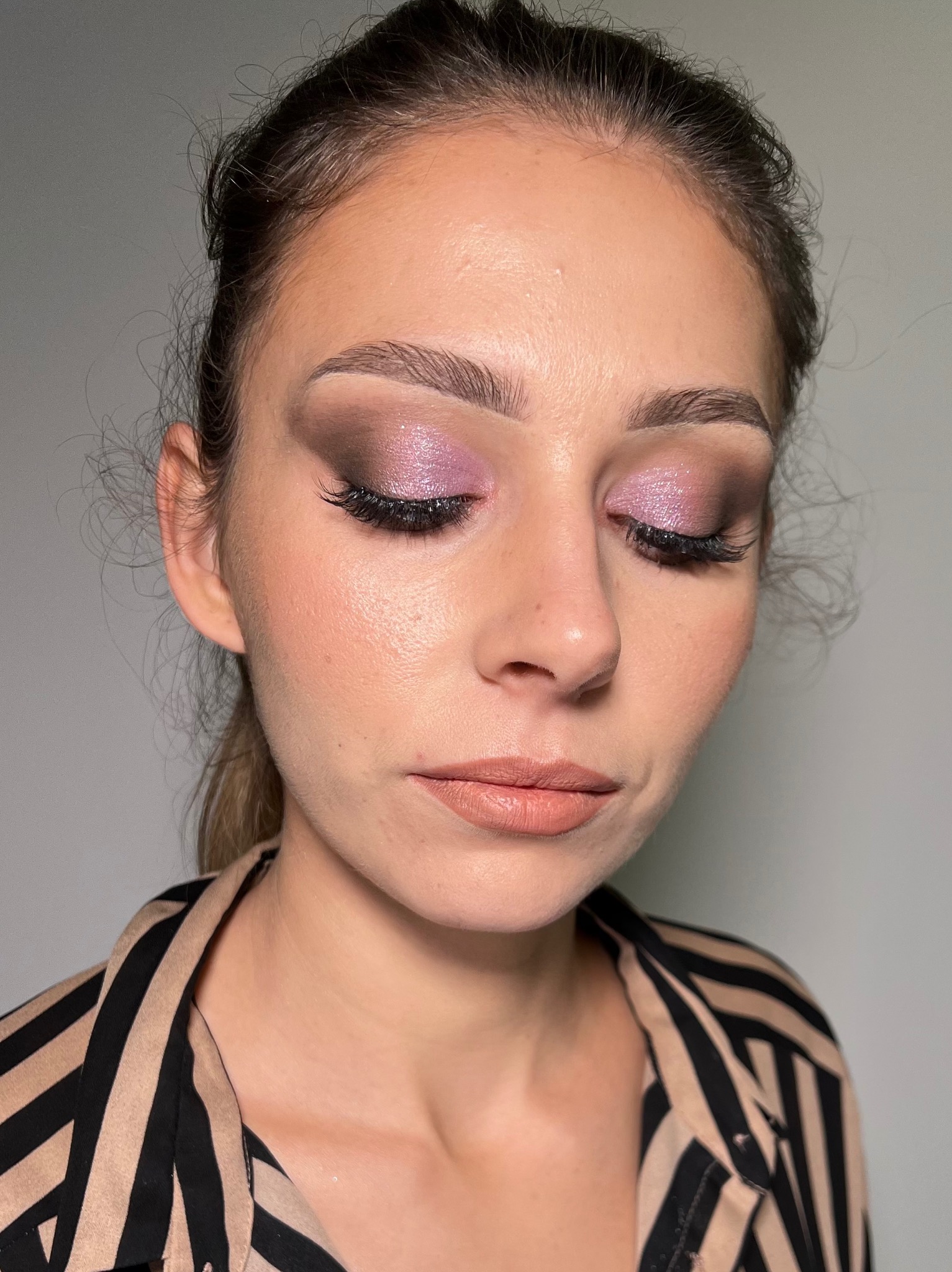 Kobieta z zamkniętymi oczami prezentuje wykonany na powiekach brokatowy, różowo-fioletowy cień, podkreślony czarną kreską i wydłużonymi rzęsami, z delikatnym konturowaniem twarzy i ustami...