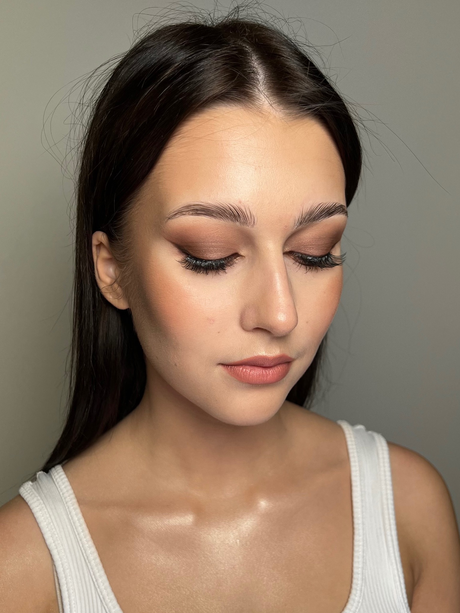 Portret kobiety z delikatnym, brązowym cieniowaniem powiek, sztucznymi rzęsami i subtelnym konturowaniem policzków, patrzącej w dół.