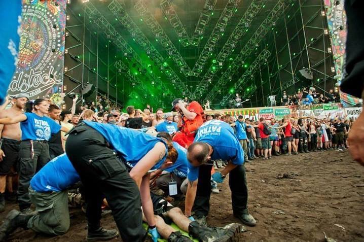 Ochrona imprezy masowej: Ratownicy medyczni udzielają pomocy osobie poszkodowanej podczas koncertu na tle sceny oświetlonej zielonymi światłami.