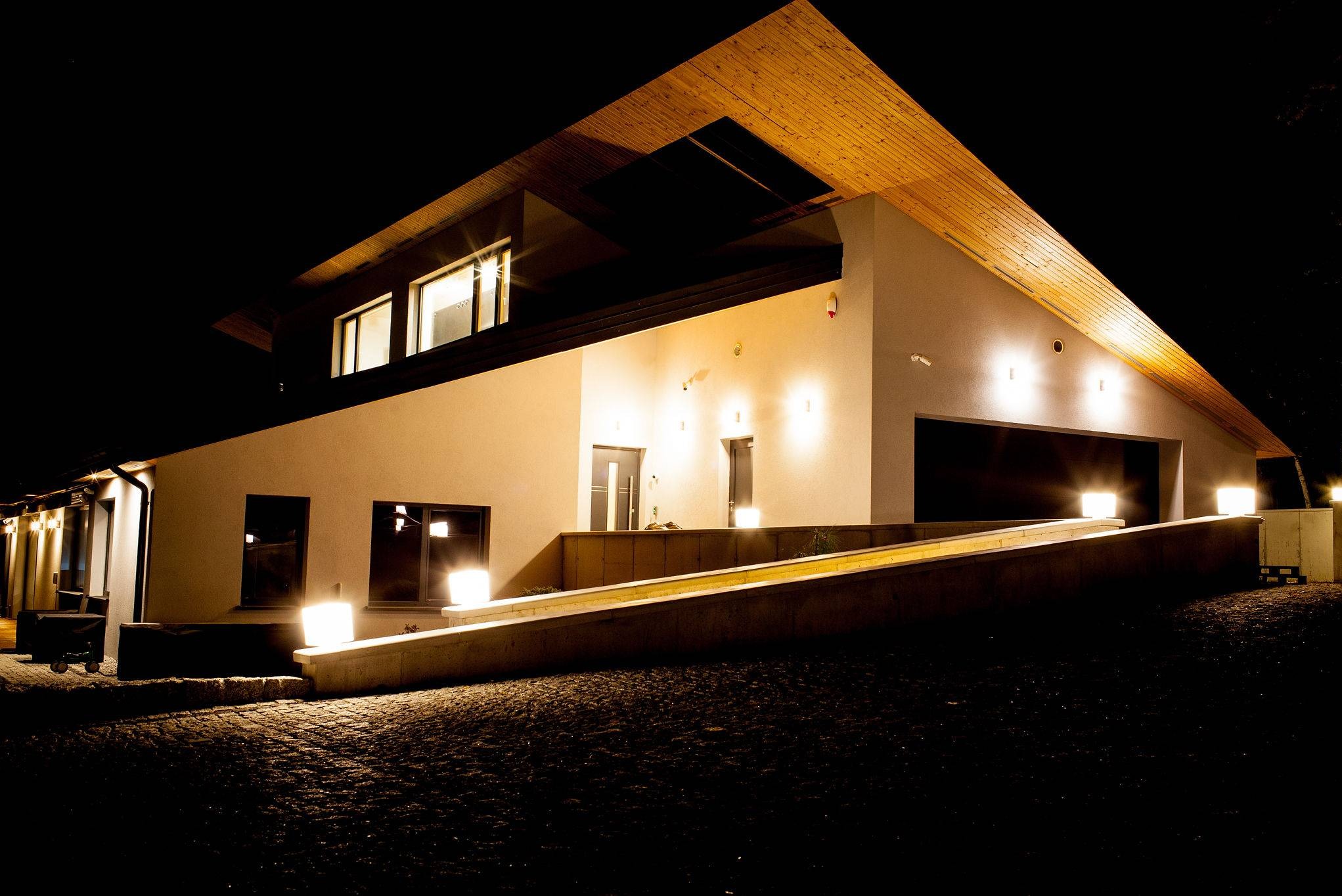 Nowoczesny dom z płaskim dachem i oświetloną rampą wjazdową, nocne ujęcie z niskiego kąta.