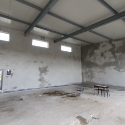 Elektryk i Tynkarz - Wnętrze hali w Żelechlinku po nałożeniu tynku cementowo-wapiennego, widoczne ślady po procesie tynkowania na ścianach, surowy stan wykończenia.