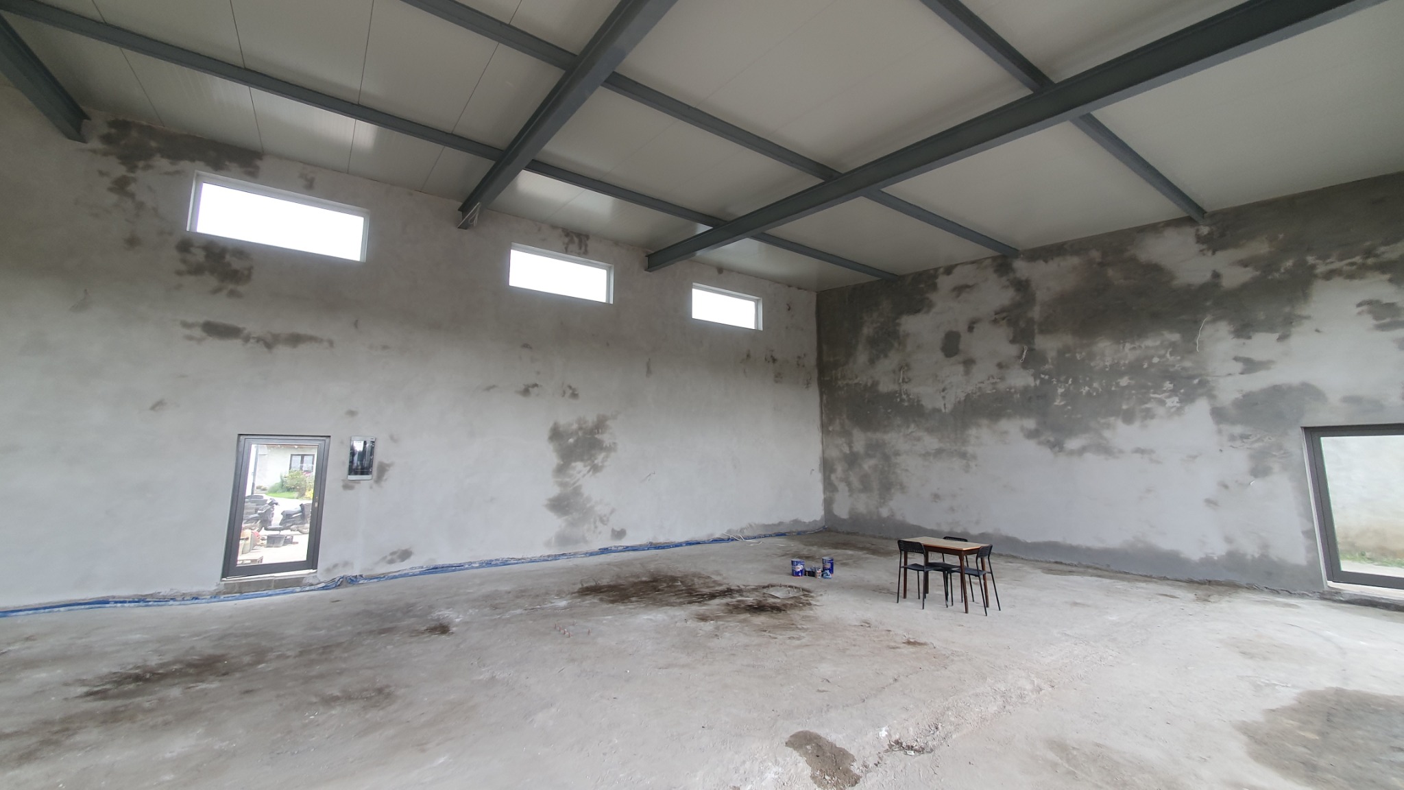 Wnętrze hali w Żelechlinku po nałożeniu tynku cementowo-wapiennego, widoczne ślady po procesie tynkowania na ścianach, surowy stan wykończenia.