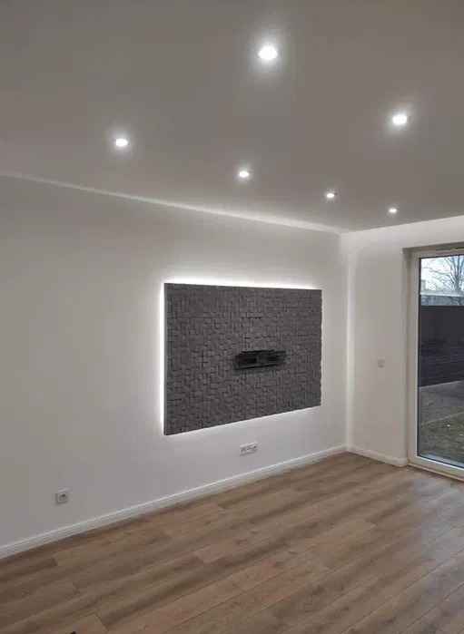 Ściana akcentowa z szarych, trójwymiarowych paneli z podświetleniem LED, zamontowana w nowocześnie wykończonym salonie z drewnianą podłogą i oknem balkonowym.