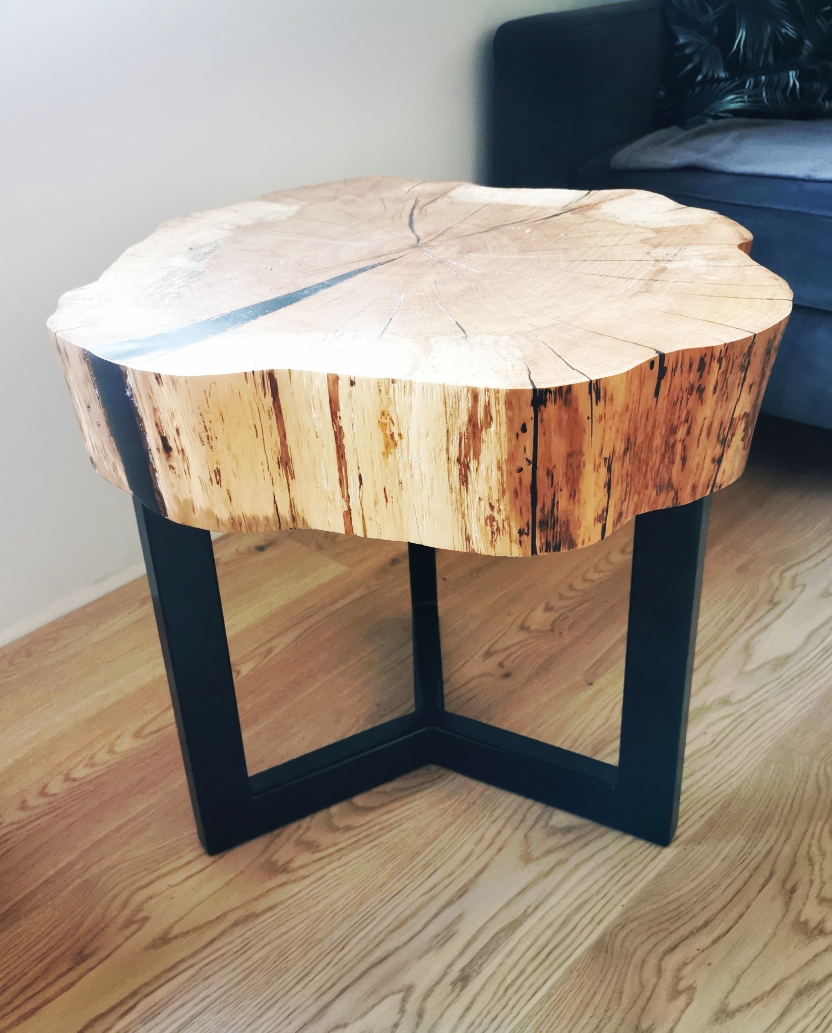 Stolik kawowy z blatem z plastra drewna z żywicą epoksydową i czarnymi, metalowymi nogami, na parkiecie.