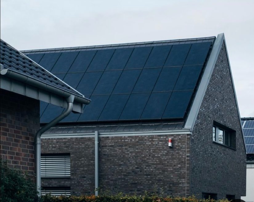 Dom jednorodzinny z ciemnej cegły z panelami na dachu, widok z dołu w pochmurny dzień.