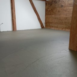 Wykończenia wnętrz - Wyrównana wylewka podłogowa w poddaszu z drewnianymi elementami konstrukcyjnymi na ścianach i suficie.