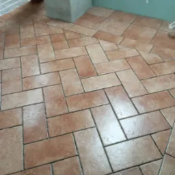 Ułożona terakota w jodełkę na podłodze łazienki w trakcie prac wykończeniowych, widoczne rury ogrzewania podłogowego i surowe ściany.