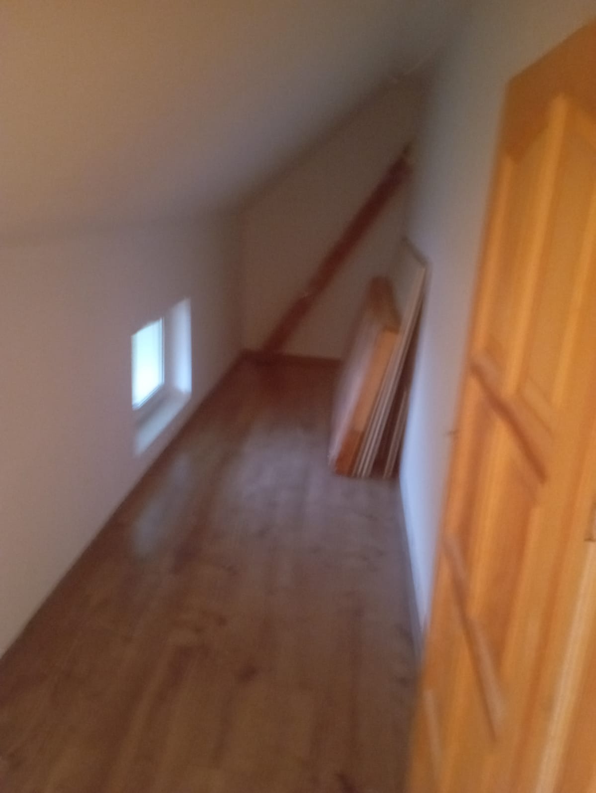 Poddasze z oknem, drewnianą podłogą i drewnianymi drzwiami, w rogu oparte o ścianę płyty.