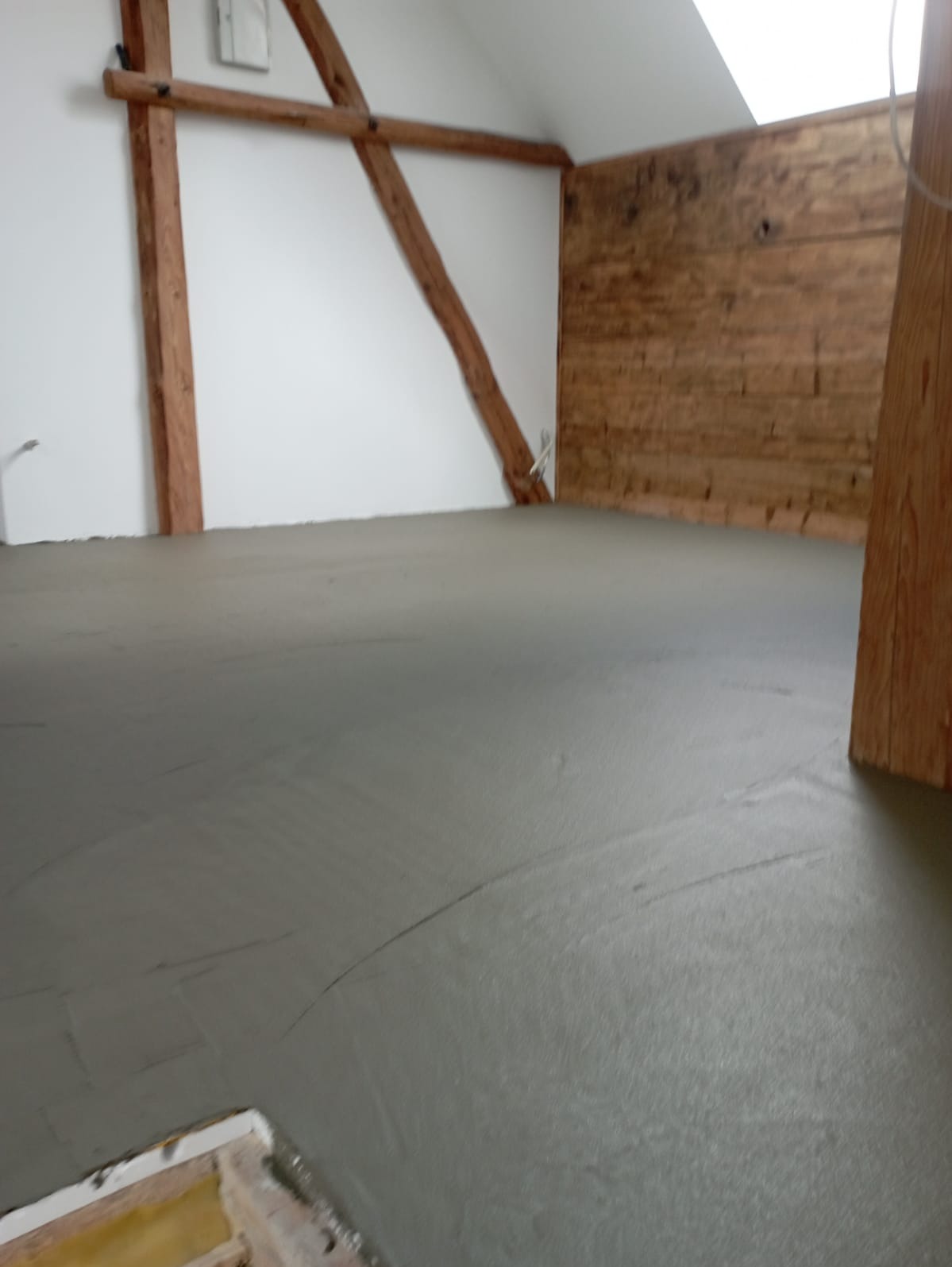 Wyrównana wylewka podłogowa w poddaszu z drewnianymi elementami konstrukcyjnymi na ścianach i suficie.