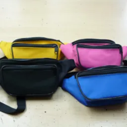 Cztery saszetki biodrowe w kolorach żółtym, różowym, czarnym i niebieskim leżą na drewnianym blacie.